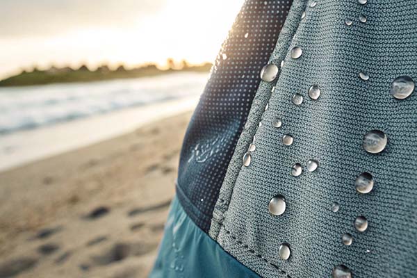 Close-up of water droplets on textured, water-resistant swimwear fabric at the beach.