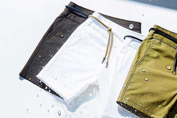 Three pairs of water-resistant shorts in black, white, and olive green, styled with water droplets for a refreshing summer look.