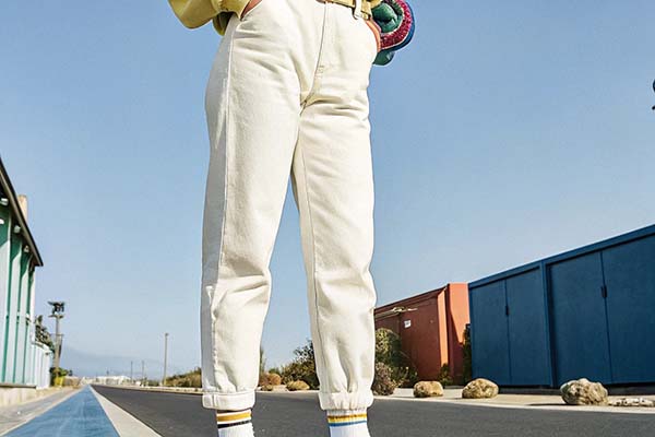 Person wearing white cuffed pants and striped socks standing on a sunny street with colorful buildings in the background.