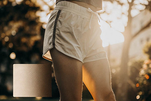 Woman wearing beige running shorts with sunlight background.