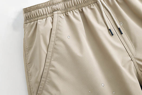 Close-up of beige swim shorts with drawstring and side pockets.