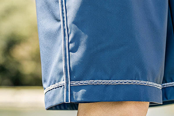 Close-up of blue shorts featuring white contrast stitching along the hem and seams.