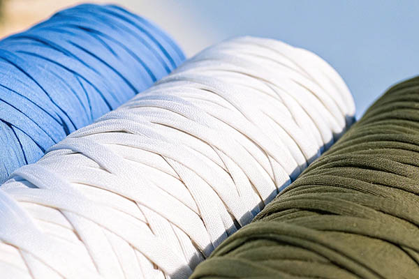Close-up of three tightly wound fabric ribbon rolls in blue, white, and green, arranged outdoors.