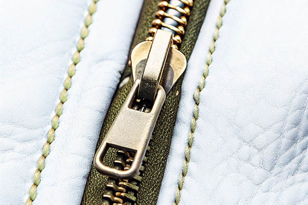 Close-up of a brass zipper on green and white textured fabric with detailed stitching.