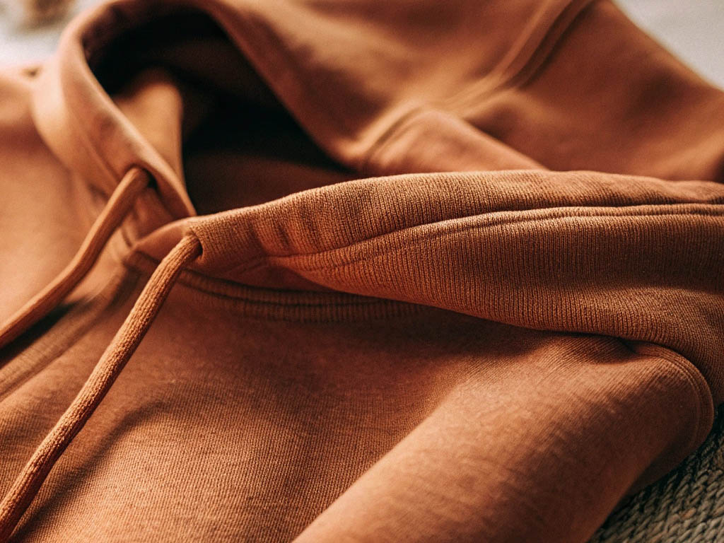 Soft brown hoodie with ribbed cuffs, visible stitching, and matching drawstrings in warm lighting.