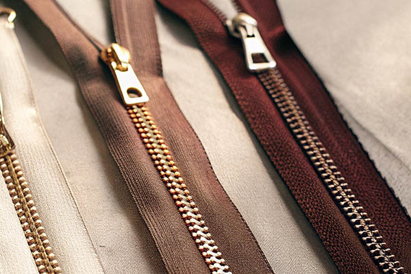 Four zippers in shades of brown with gold and silver metal teeth on fabric.