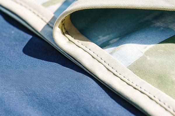 Detailed view of stitched fabric edges in blue and patterned beige, highlighting texture and craftsmanship.