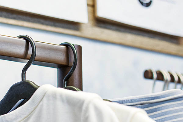 Close-up of white and striped shirts hanging on black hangers from a wooden clothing rack.