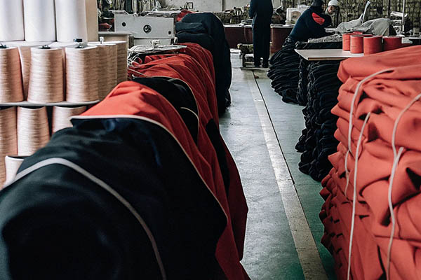 Stacks of red and black garments alongside large thread spools in a busy clothing production facility.