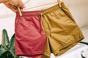 Hand holding red and yellow shorts on a hanger indoors.