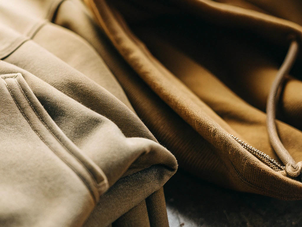 Close-up of two hoodies in earthy tones, highlighting fabric texture, stitching, and drawstrings.