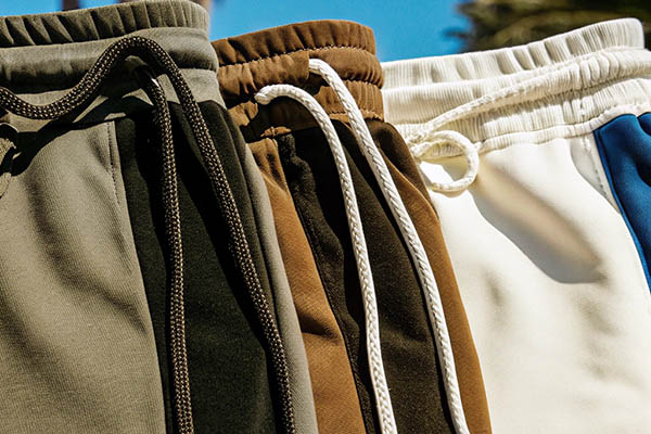 Multiple pairs of drawstring shorts in earthy tones and white with blue accents hanging outdoors.