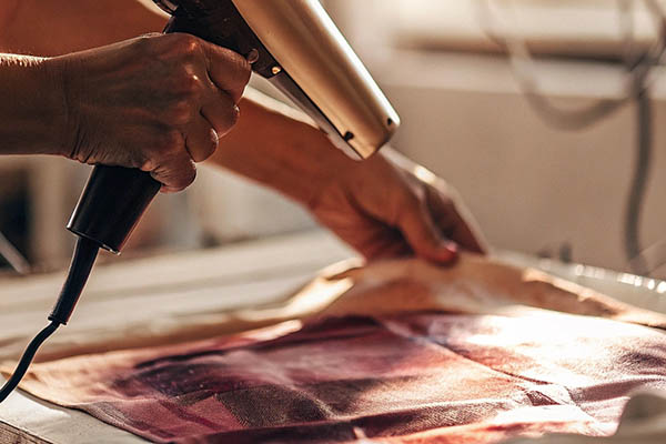Person using heat gun to set ink on fabric print.