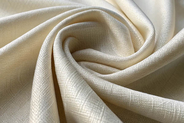Close-up of cream-colored fabric with a subtle textured pattern, artistically draped in soft folds.