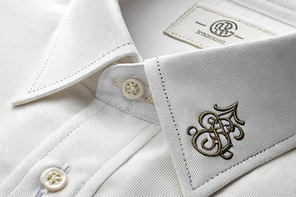 Close-up of a luxury white dress shirt with intricate gold embroidery on the collar and elegant button details.