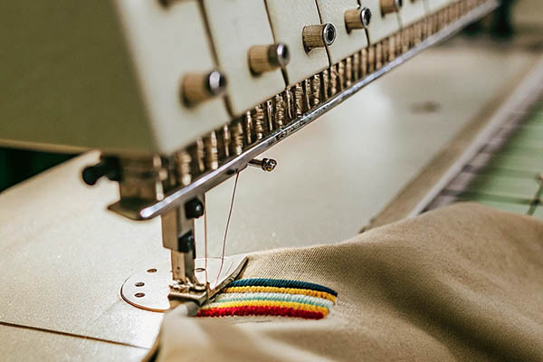 Industrial embroidery machine stitching colorful stripes on beige fabric.