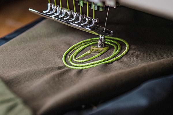 Close-up of an embroidery machine stitching a green spiral pattern onto dark fabric with precision.