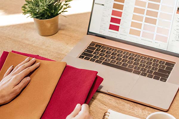 A person comparing fabric swatches with a digital color palette on a laptop, selecting shades for design.
