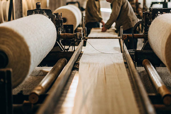 Textile factory with fabric rolls on machines and workers in the background.