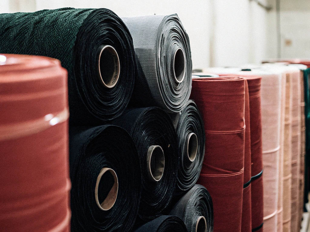 Stacked rolls of colored fabric in a warehouse setting.
