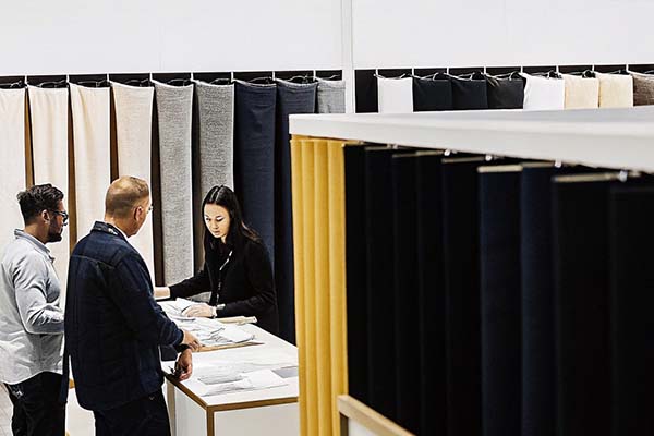 Business professionals discussing fabric samples at a textile exhibition with fabric rolls displayed.