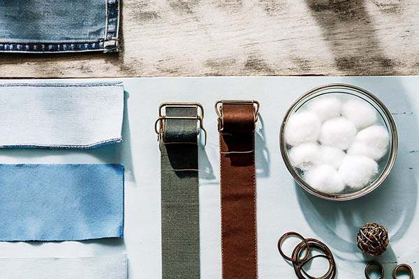 Light blue fabric swatches, belts, cotton balls, and metal rings arranged on a wooden surface with natural lighting.