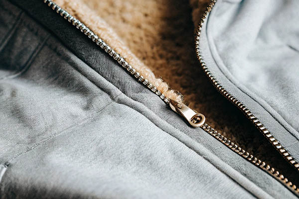 Gray hoodie with a silver zipper and soft beige fleece lining, highlighting stitching details.