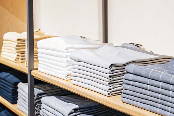 Neatly stacked white, gray, and blue folded shirts on wooden shelves in a retail store.