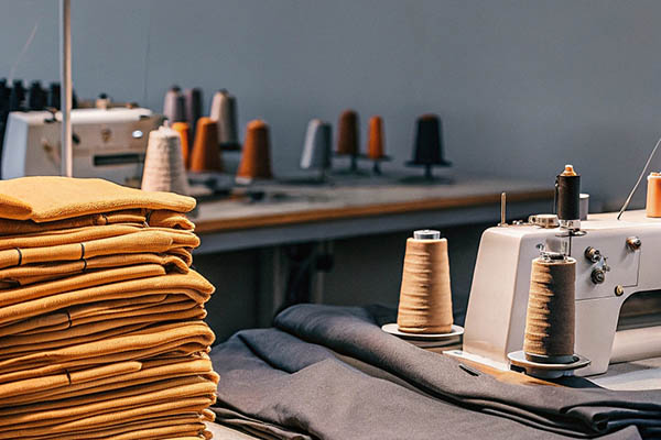Stacked yellow and gray fabrics beside sewing machines with colorful thread spools in a workshop.