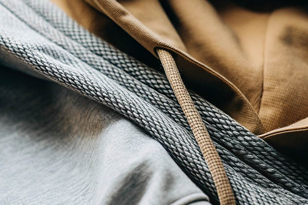 Close-up of gray and brown hoodies with thick, textured drawstrings and soft fabric.
