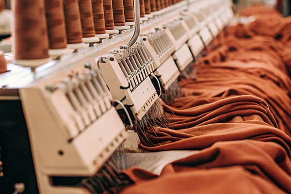 A row of embroidery machines stitching rust-colored fabric with matching thread spools above.