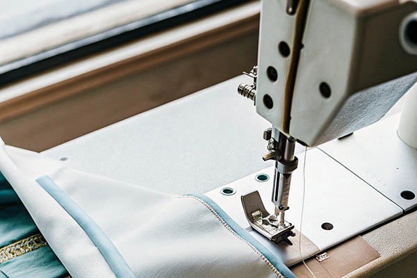 Close-up of sewing machine stitching light blue fabric.