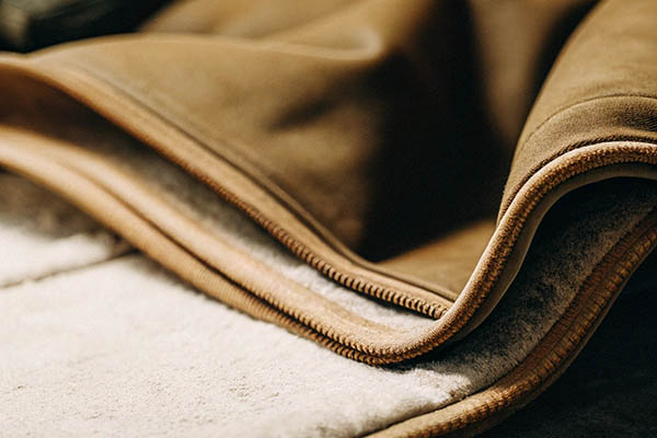 Close-up of brown fabric with soft, white fleece lining and stitched edges.