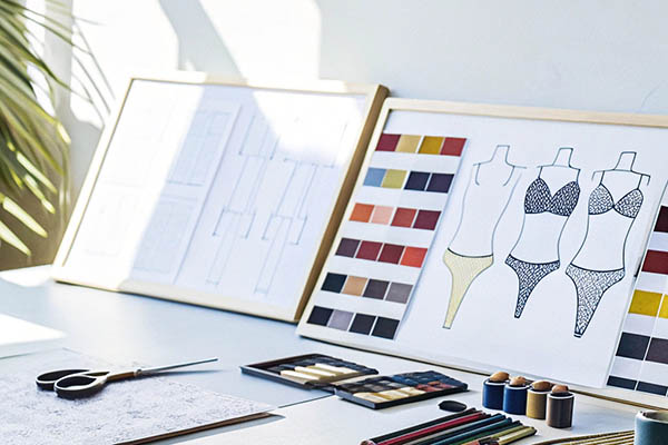 Lingerie sketches, color palettes, and design tools on a desk.