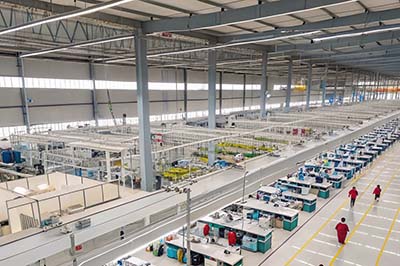 A large textile factory with multiple sewing stations, organized workspaces, and workers in red uniforms assembling garments.