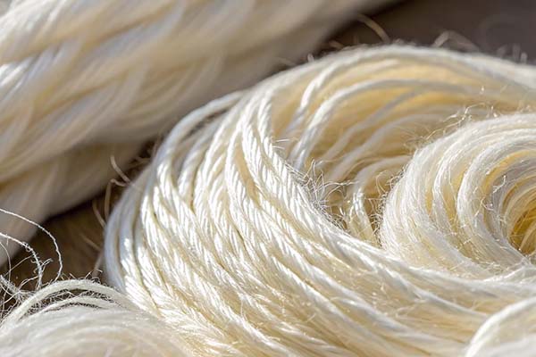 Close-up of raw, twisted natural fiber threads in a soft, off-white color, highlighting texture and detail.
