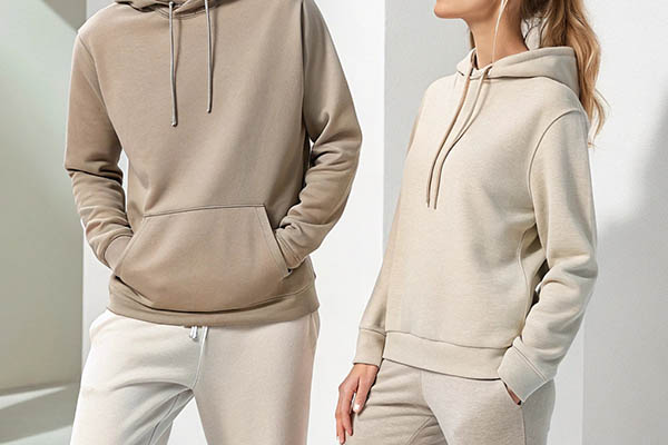 Two models wearing beige and cream hoodies with drawstrings and front pockets.