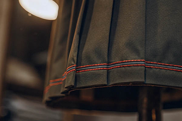 Close-up of dark pleated skirt with red stitched hem detailing.