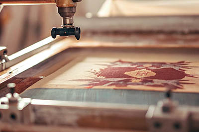 Close-up of a screen printing machine applying a design onto fabric in a workshop.