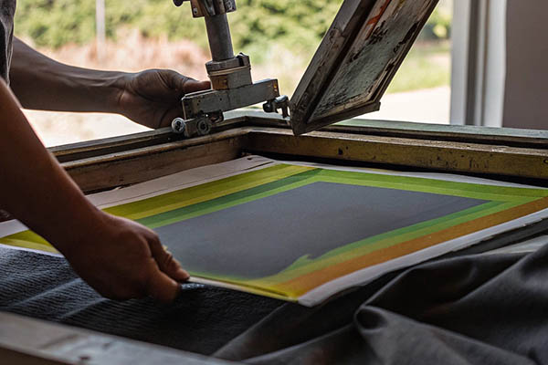 Person manually operating screen printing equipment on fabric.