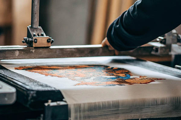 Close-up of a worker using a screen printing machine to apply a colorful design on fabric.