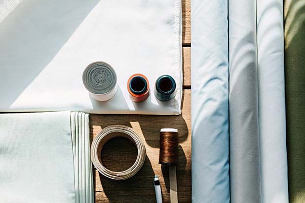 White and pastel fabric rolls, threads, measuring tape, and sewing tools on a wooden surface.