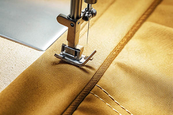 Sewing machine needle stitching yellow fabric with precise seams.