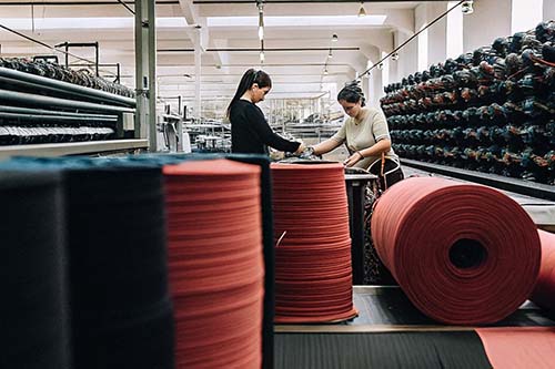 Workers handling large rolls of fabric in a textile production facility with machinery.