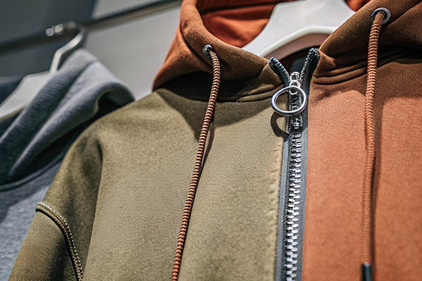 Close-up of a two-tone hoodie with green and brown panels, silver zipper, and matching drawstrings.
