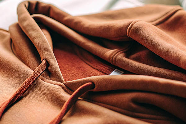 Close-up of a brown hoodie with soft fabric texture, visible stitching, and matching drawstrings.