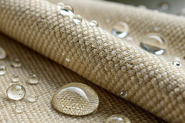 Close-up of beige woven fabric with water droplets beading on the surface.