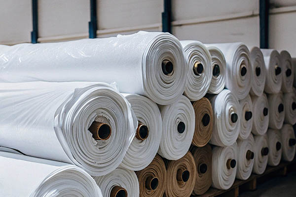 Stacked rolls of white and beige fabric on pallets.