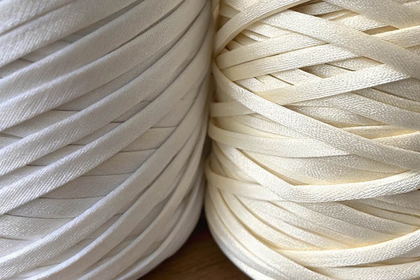 Close-up of two tightly wound fabric ribbon rolls in white and cream, showcasing their smooth texture.