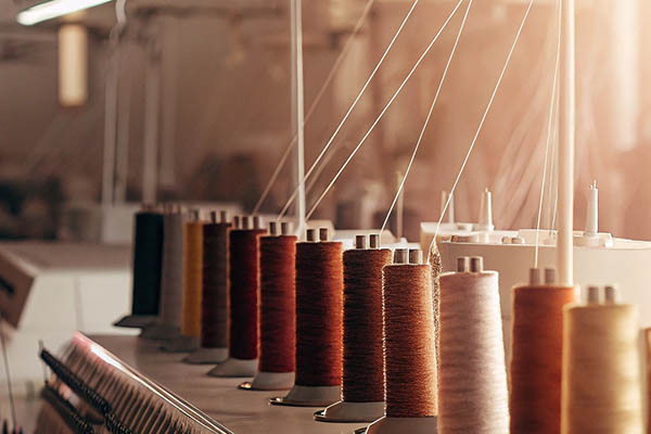 Rows of colorful yarn spools on industrial textile machines.